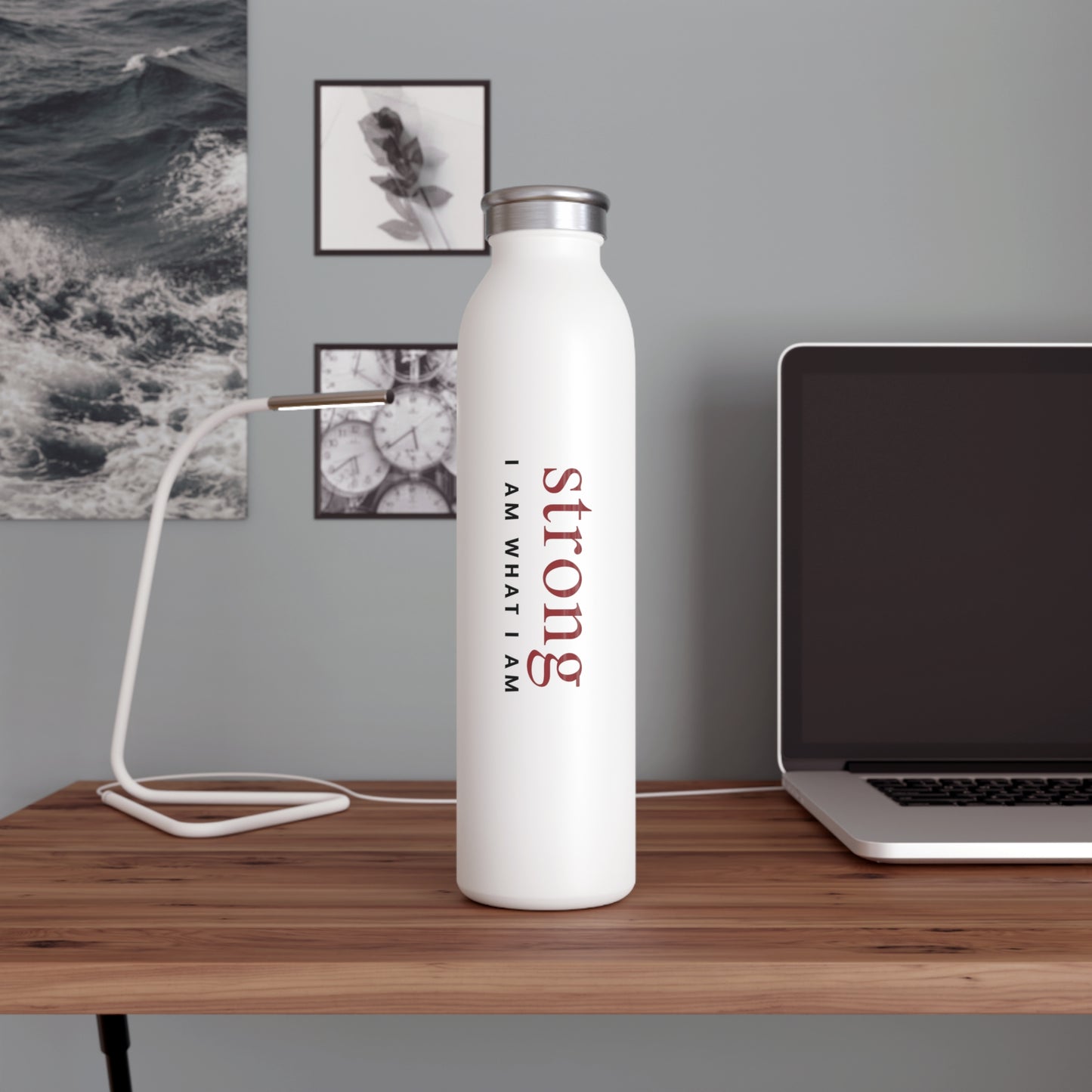  White water bottle with 'strong I AM WHAT I AM' text on a wooden desk with a laptop and lamp.