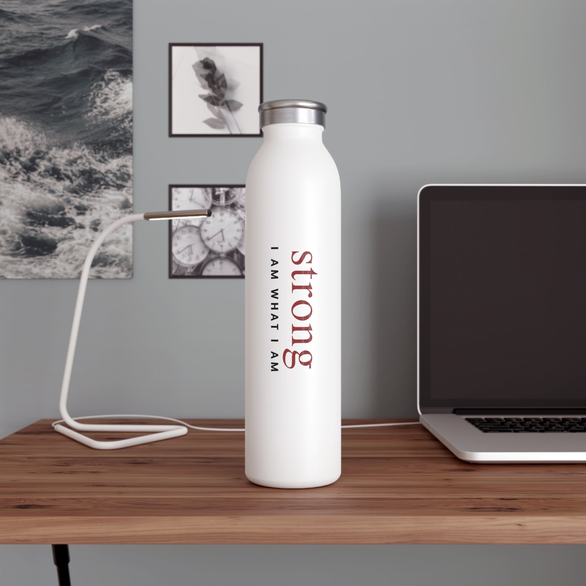  White water bottle with 'strong I AM WHAT I AM' text on a wooden desk with a laptop and lamp.