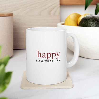 White mug with 'happy I AM WHAT I AM' text on a coaster, surrounded by plants and a bowl of fruit.